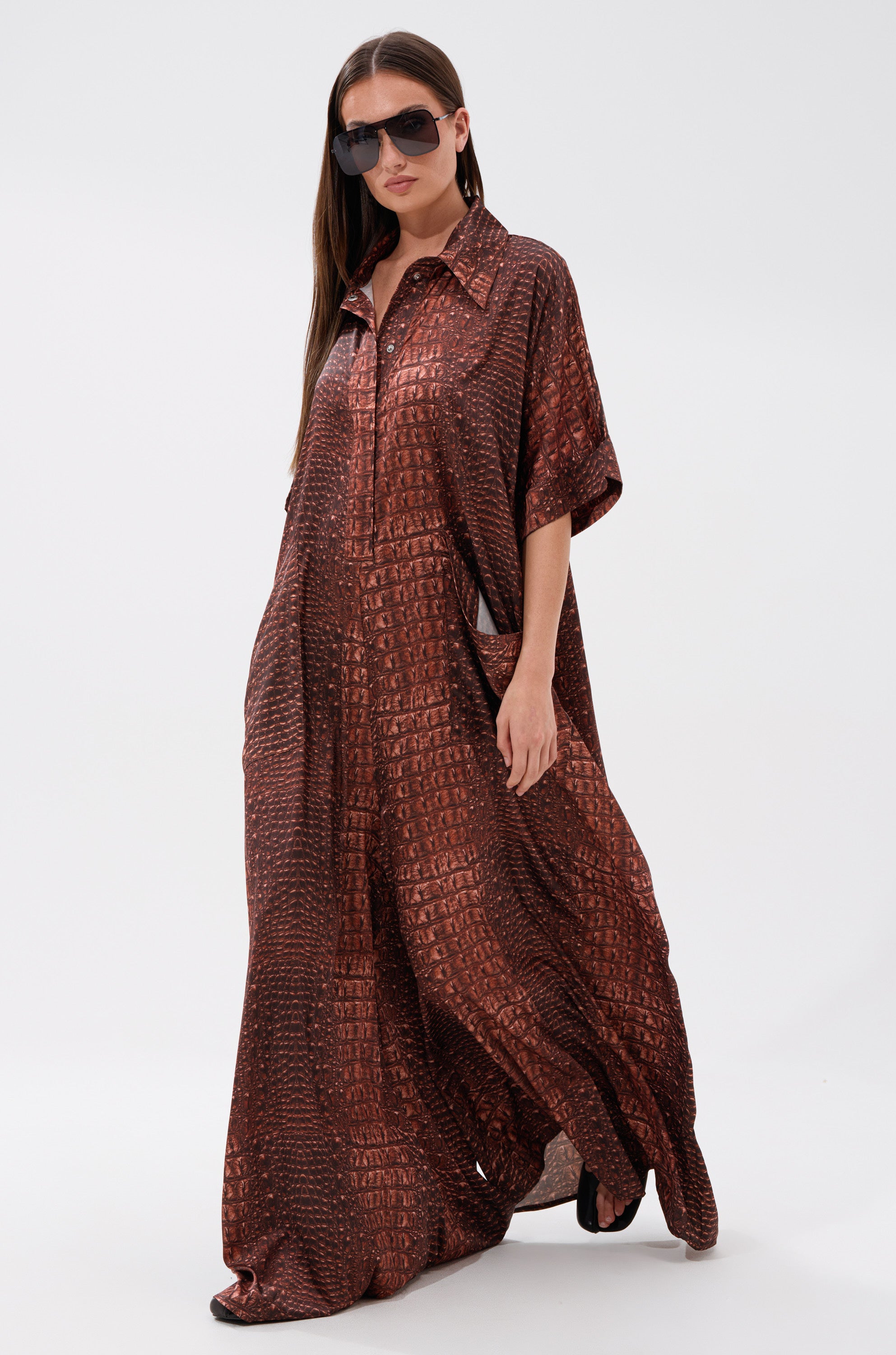 A woman in an oversized satin jumpsuit featuring a brown crocodile print.