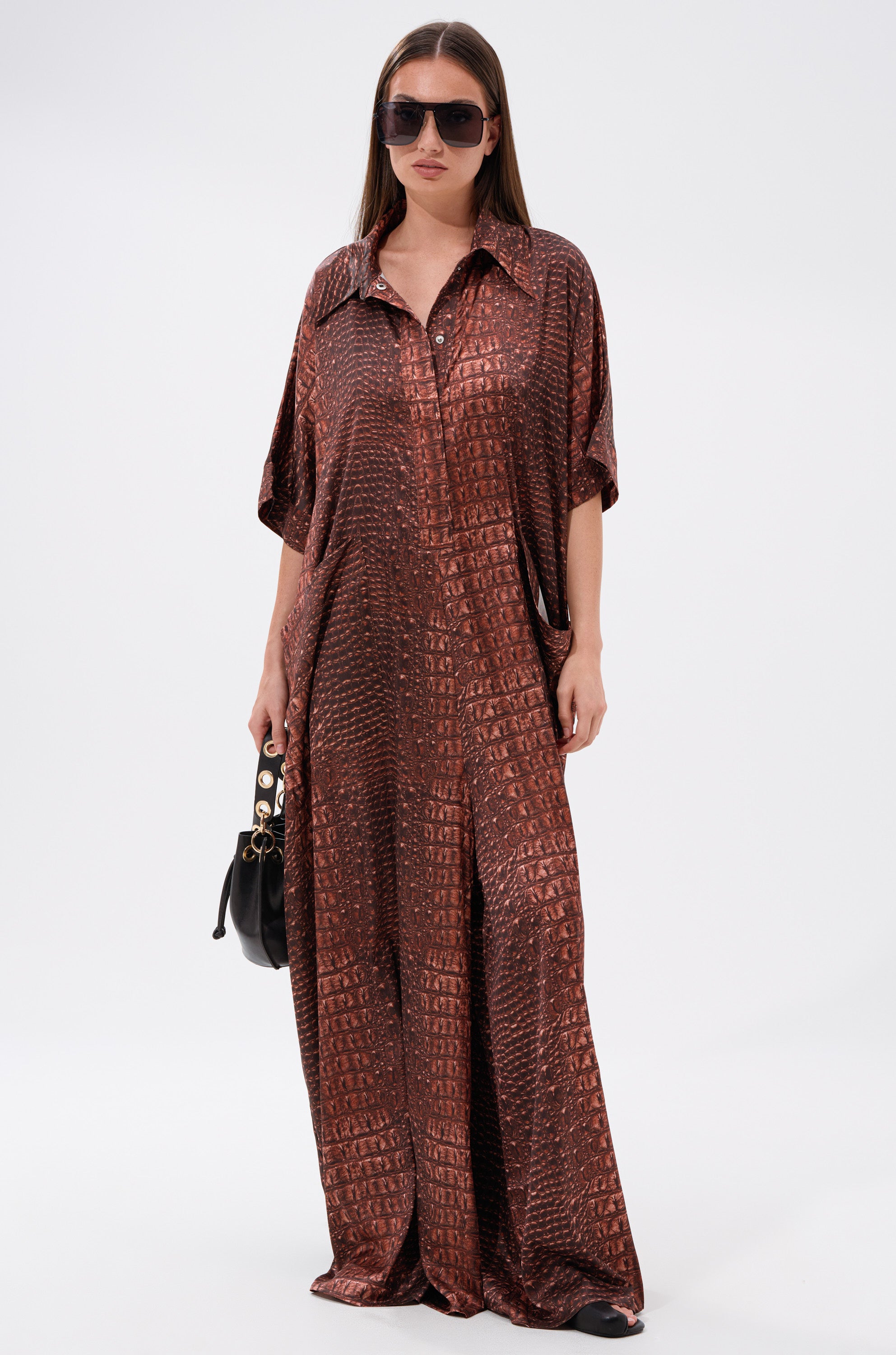 A woman wearing oversized sunglasses and the SHE'S RICH OVERSIZED SATIN JUMPSUIT IN CROC PRINT stands against a plain white background, holding a small black handbag.