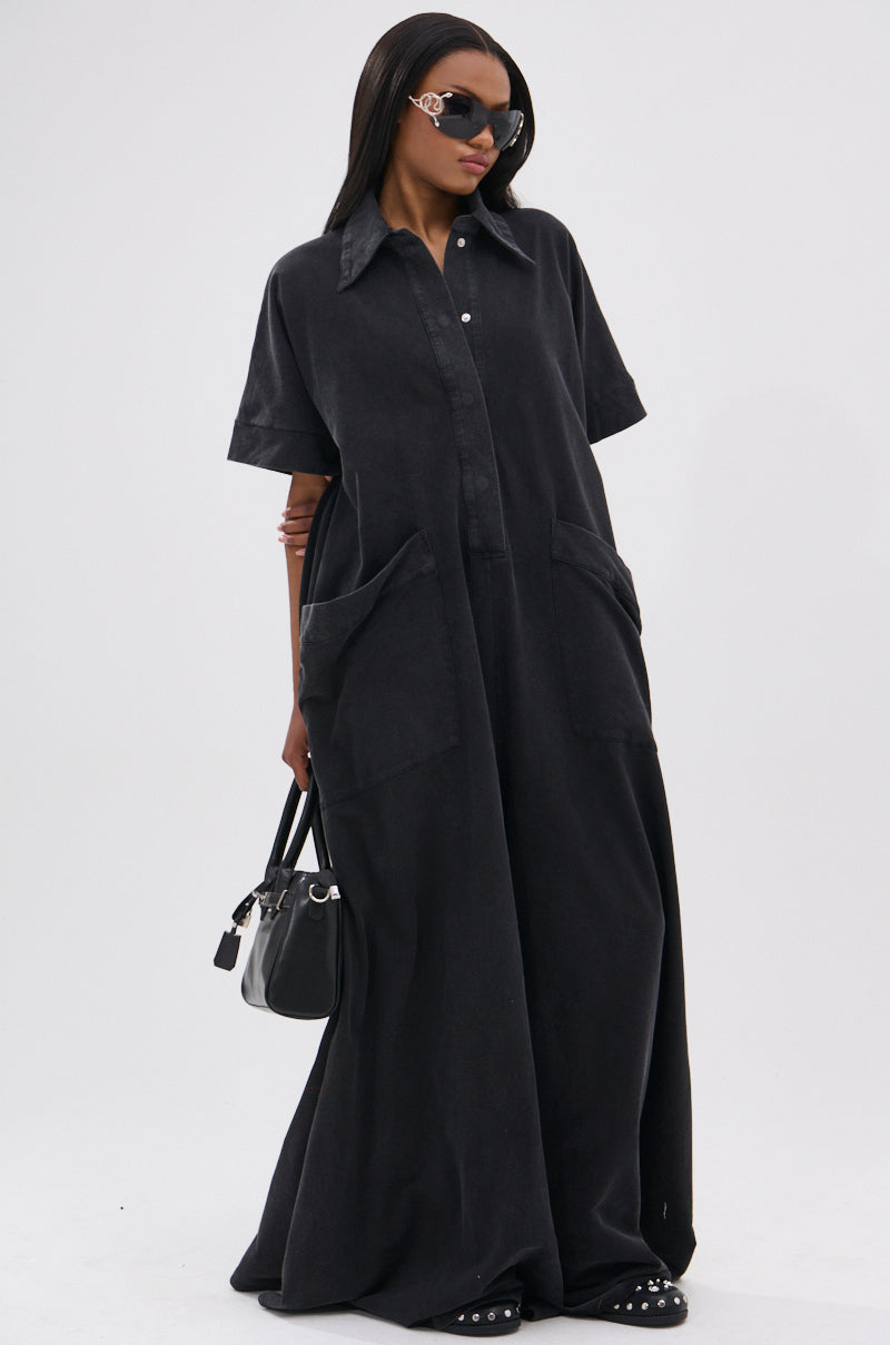A woman wears the HAPPY HOUR FRENCH TERRY JUMPSUIT, featuring a relaxed fit and short sleeves, styled with black sandals, sunglasses, a black-and-white handbag, and multiple bracelets on one arm.