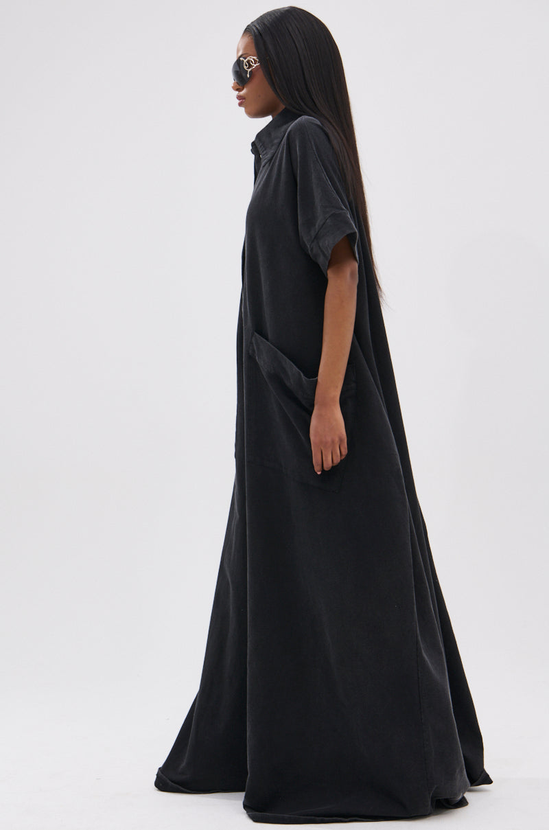 A woman with long straight hair and sunglasses stands in profile against a plain white background, wearing the loose, floor-length, oversized HAPPY HOUR FRENCH TERRY JUMPSUIT featuring short sleeves and large pockets.