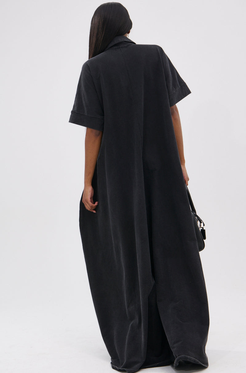 A person with long, straight hair faces away from the camera, wearing a loose-fitting, floor-length black HAPPY HOUR FRENCH TERRY JUMPSUIT made of semi-stretchy knit cotton and holding a black handbag against a plain white background.