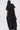 A person with long, straight hair faces away from the camera, wearing a loose-fitting, floor-length black HAPPY HOUR FRENCH TERRY JUMPSUIT made of semi-stretchy knit cotton and holding a black handbag against a plain white background.