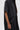 A person wears the HAPPY HOUR FRENCH TERRY JUMPSUIT, a loose-fitting, short-sleeved, dark grey button-up piece with large front pockets and an oversized silhouette, against a plain light background. Only the upper body and one arm are visible.