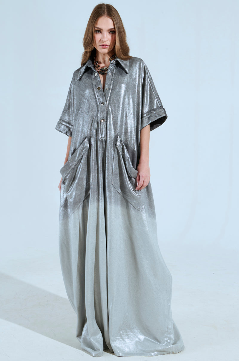 A woman dons the LIFE GOES ON OMBRE FRENCH TERRY JUMPSUIT, featuring buttons, large pockets, short sleeves, and a collar. Her long, wavy brown hair cascades as she stands against a plain light background.