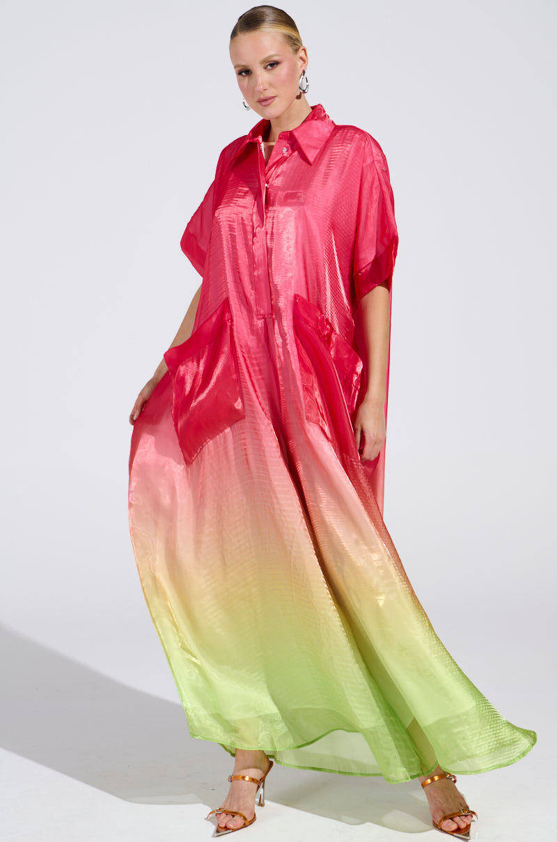 Wearing the ISLA Ombre Oversized Satin Jumpsuit in pink, transitioning from red to light green, an individual poses against a plain background. The look is enhanced with hoop earrings and strappy heeled sandals.