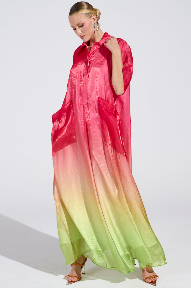 Against a plain background, a person with short blonde hair wears the ISLA Ombre Oversized Satin Jumpsuit in pink featuring large pockets and a striking gradient from red to green.