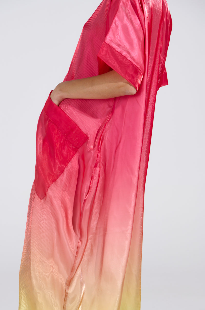 Someone is wearing the ISLA Ombre Oversized Satin Jumpsuit, featuring short sleeves and a silky transition from bright pink to pale yellow with a side pocket, set against a neutral background.