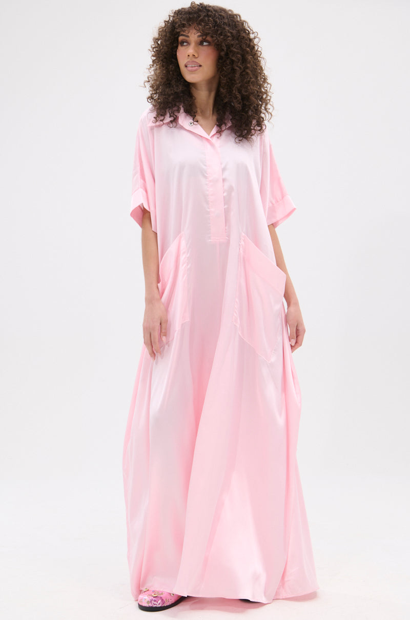 A woman with curly hair models the SHE'S RICH OVERSIZED SATIN JUMPSUIT IN LIGHT PINK, showcasing chic vacation style against a plain white background.