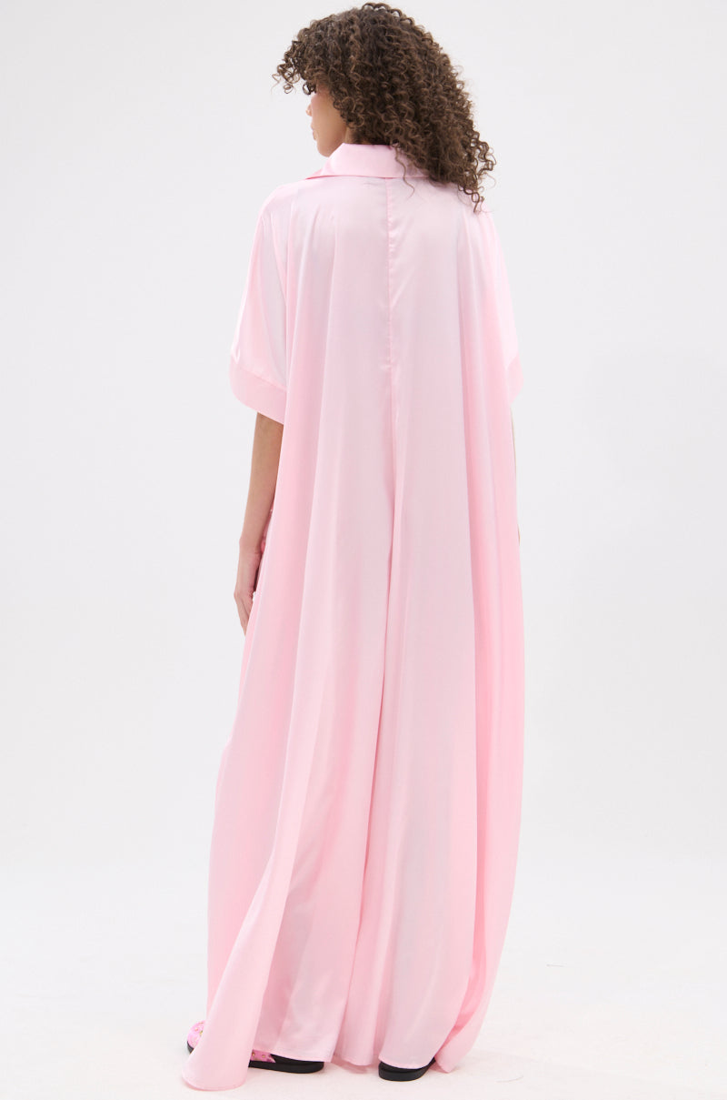 A person with curly hair faces away in the SHE'S RICH OVERSIZED SATIN JUMPSUIT IN LIGHT PINK, showcasing luxurious loungewear against a plain white background.