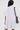 Seen from the back, a person with long, straight dark hair wears the SHE'S RICH OVERSIZED FRENCH TERRY ROMPER in light gray for all-day comfort, paired with a black shoulder bag with gold hardware against a plain light background.