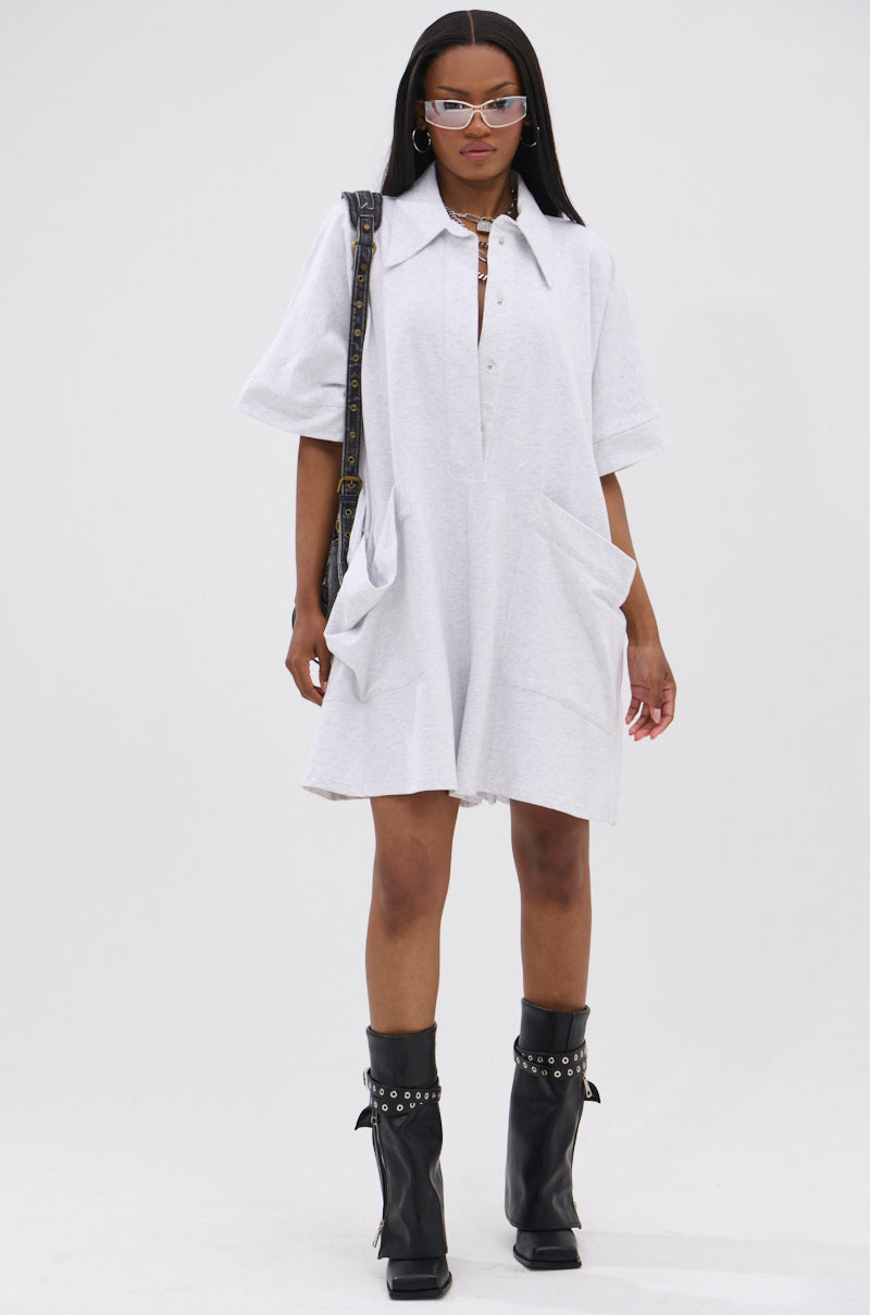 A woman in the SHE'S RICH OVERSIZED FRENCH TERRY ROMPER, styled with black knee-high boots with silver studs, sunglasses, and a shoulder bag, stands against a plain white background.