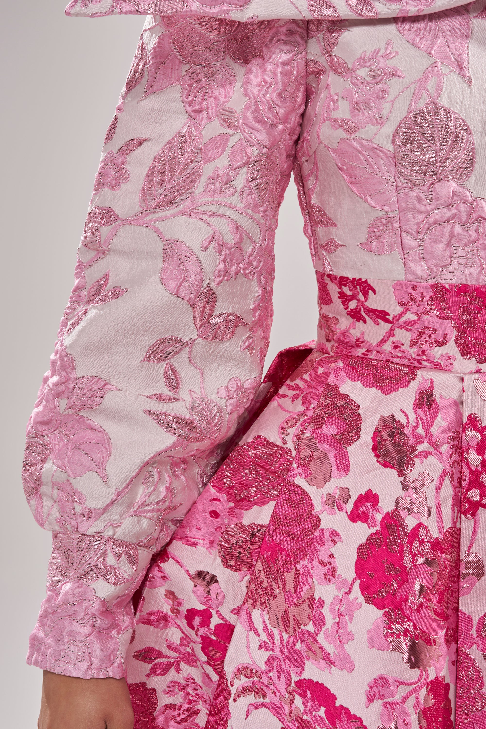 Someone wearing the RENAISSANCE TWO-TONE BROCADE MINI DRESS IN PINK, featuring long sleeves, a fitted waist, textured brocade fabric, intricate patterns, and detailed embroidery in varying shades of pink. 5