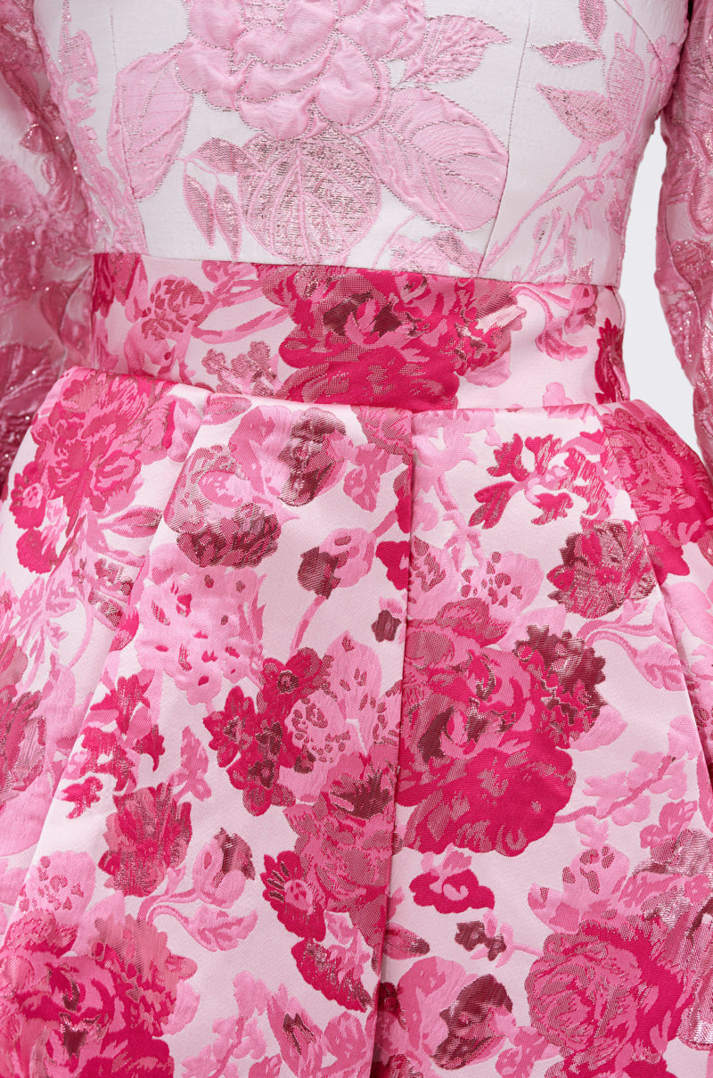 Close-up of the RENAISSANCE TWO-TONE BROCADE MINI DRESS IN PINK, featuring intricate pink and red floral embroidery, a fitted waist, pleated skirt, glossy fabric, and a sculptural bow for an elegant textured finish.