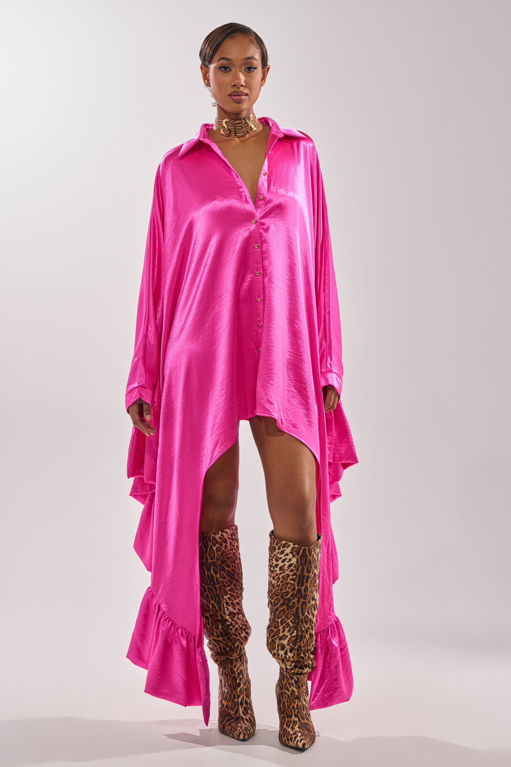 A woman poses against a plain background in the WONDERLUST Satin Long Sleeve Mini Dress in Pink, styled with leopard print knee-high boots and a gold choker for a standout look. 2