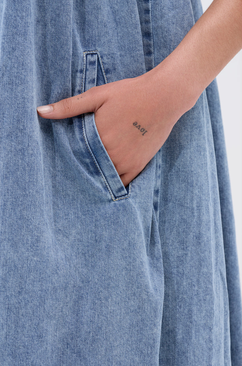 A close-up of a person's hand with a small finger tattoo, tucked into the pocket of the DIANE Strapless Oversized Jumpsuit in Denim.
