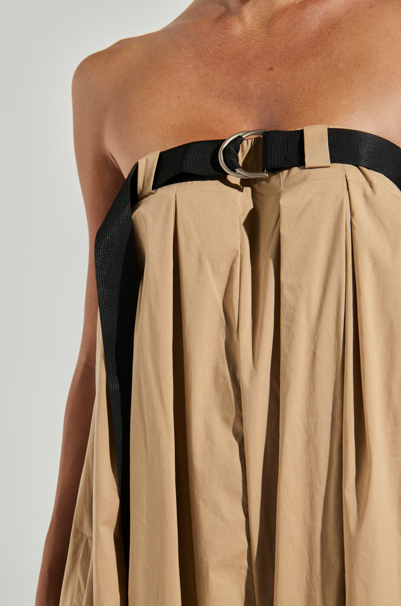 Close-up of a person wearing the DIANE STRAPLESS OVERSIZED JUMPSUIT, featuring pleats and a black belt with a silver buckle at the top edge. The belt cinches the fabric, creating a structured yet soft draping effect, evocative of an elegant strapless dress. The background is plain and light-colored.