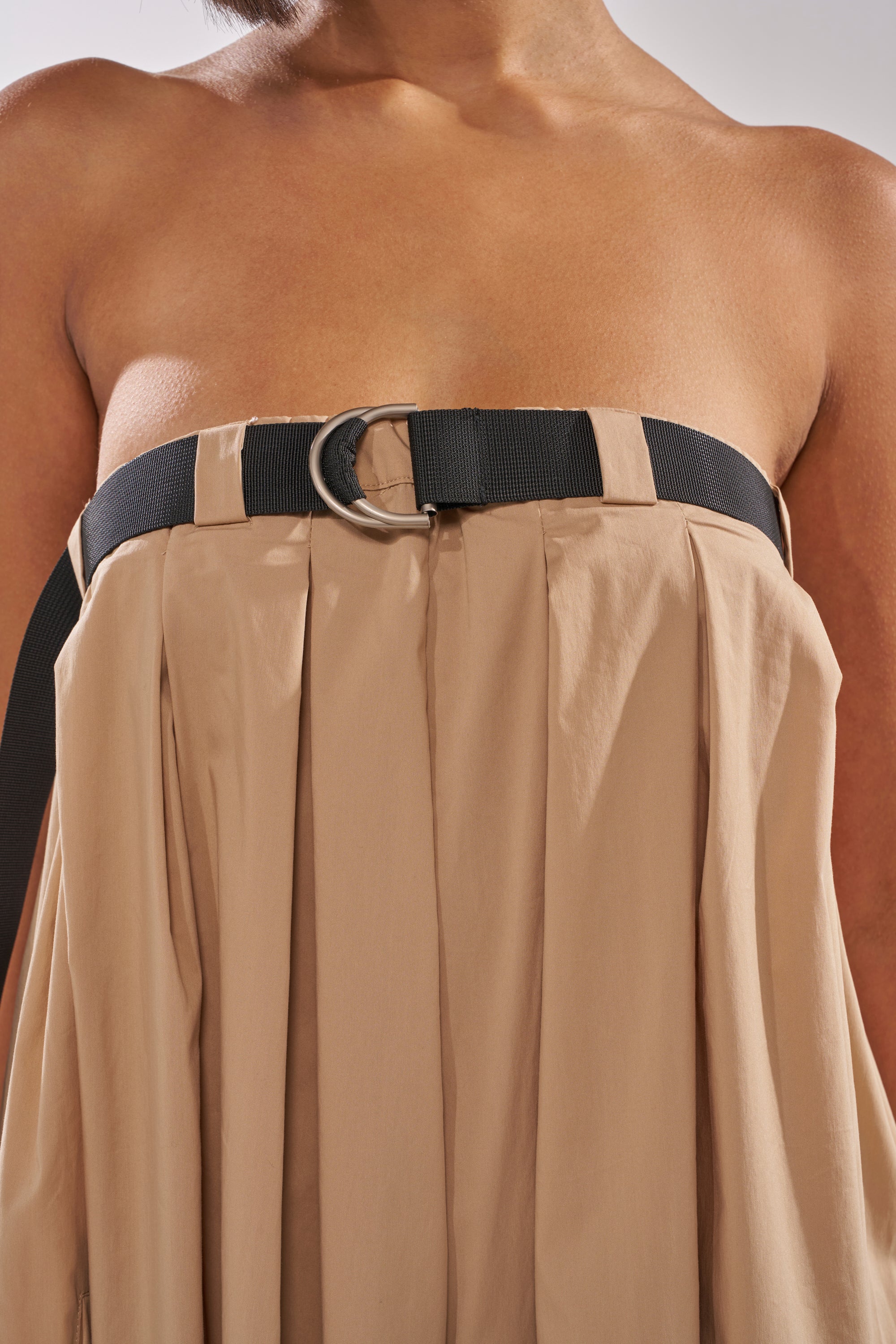 A close-up shows a person in the DIANE STRAPLESS OVERSIZED KHAKI JUMPSUIT with pleats, styled with a wide black belt and silver D-ring buckle, revealing their shoulders and upper chest. 8