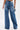 Facing away, a person wears MY OWN THING STUDDED DENIM high-rise, wide-leg blue jeans with back pocket chain details and holds a small silver bag, all set against a plain white background.