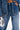 Wearing the MY OWN THING STUDDED DENIM blue jacket and matching high-rise wide-leg jeans, a person holds a shiny silver clutch, showing off a tattoo on their exposed midriff.