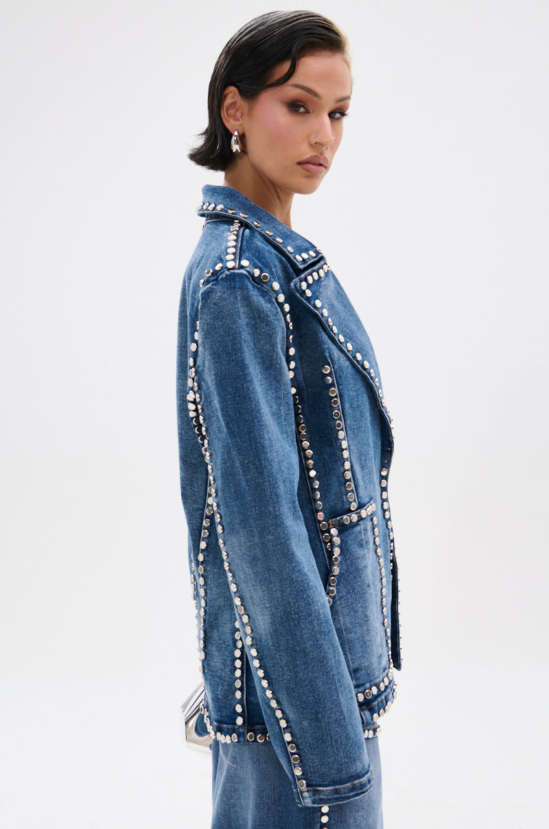 A woman with short dark hair models the MY OWN THING STUDDED DENIM BLAZER with a notched lapel collar, matching denim pants, and silver earrings, posing against a plain white background.