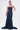 A woman stands against a plain white background, holding a small handbag and wearing the LUNA DENIM MAXI DRESS—a dark-wash, strapless maxi dress with a fitted bodice.