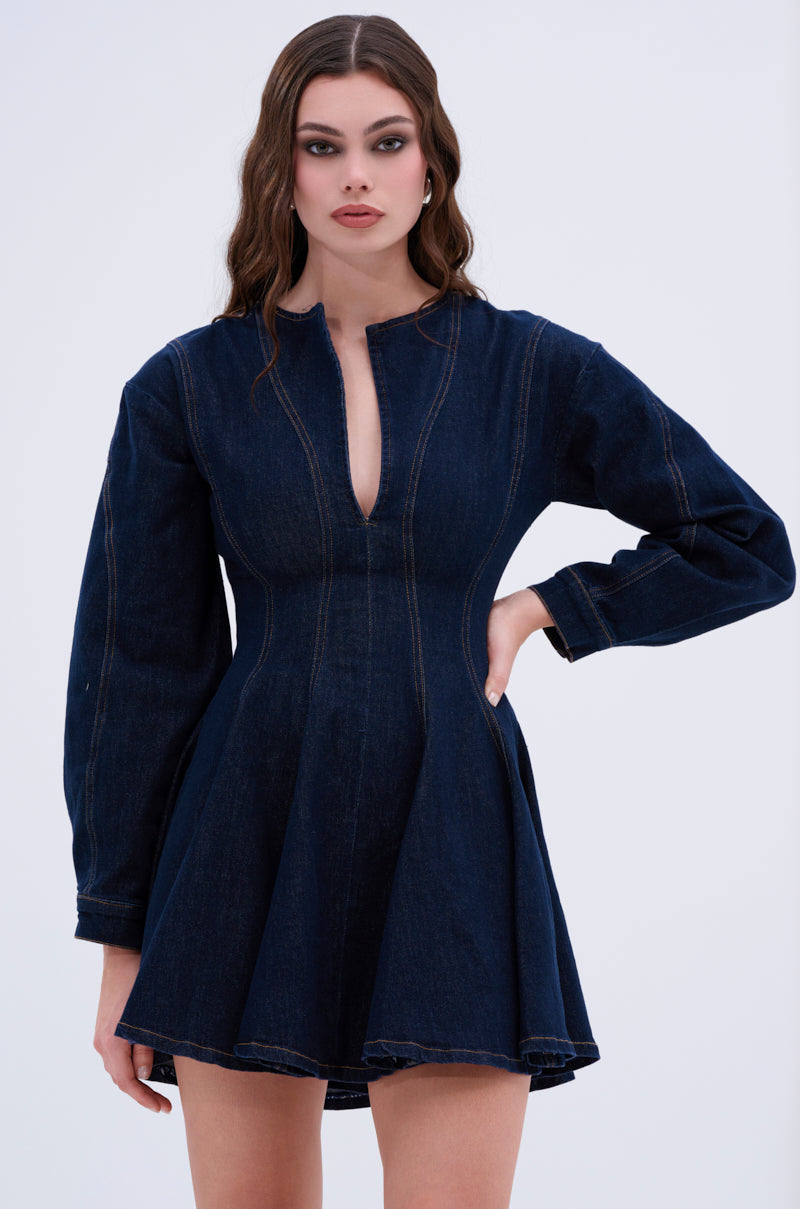 The ALL ABOUT MY BUSINESS DENIM MINI DRESS in dark blue showcases long sleeves and a V-shaped neckline. It features a skater silhouette, fitted at the waist and slightly flaring out. The neutral background highlights its chic design.