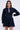 The ALL ABOUT MY BUSINESS DENIM MINI DRESS in dark blue showcases long sleeves and a V-shaped neckline. It features a skater silhouette, fitted at the waist and slightly flaring out. The neutral background highlights its chic design.