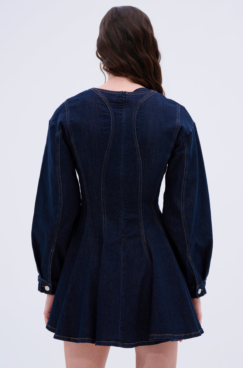 A person with long brown hair is seen from behind, showcasing the ALL ABOUT MY BUSINESS DENIM MINI DRESS IN DARK BLUE. This dress features a skater silhouette with long sleeves, a flared skirt, visible stitching, and buttoned cuffs against a plain white background.