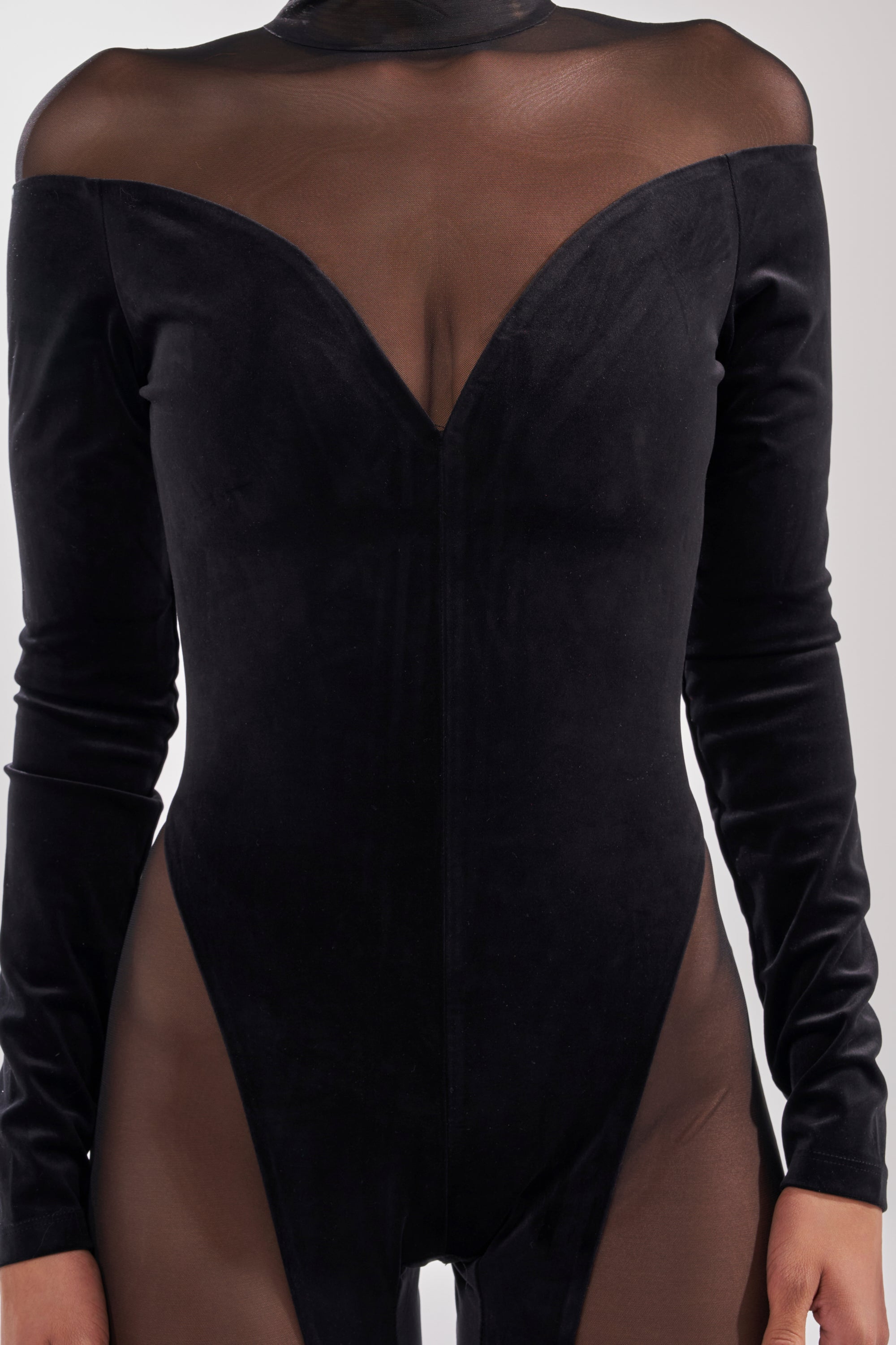A person wears the MESH TO IMPRESS LONG SLEEVE JUMPSUIT, featuring sheer black mesh panels, long sleeves, and an off-shoulder design. The form-fitting jumpsuit highlights the silhouette. The head is not visible. 5