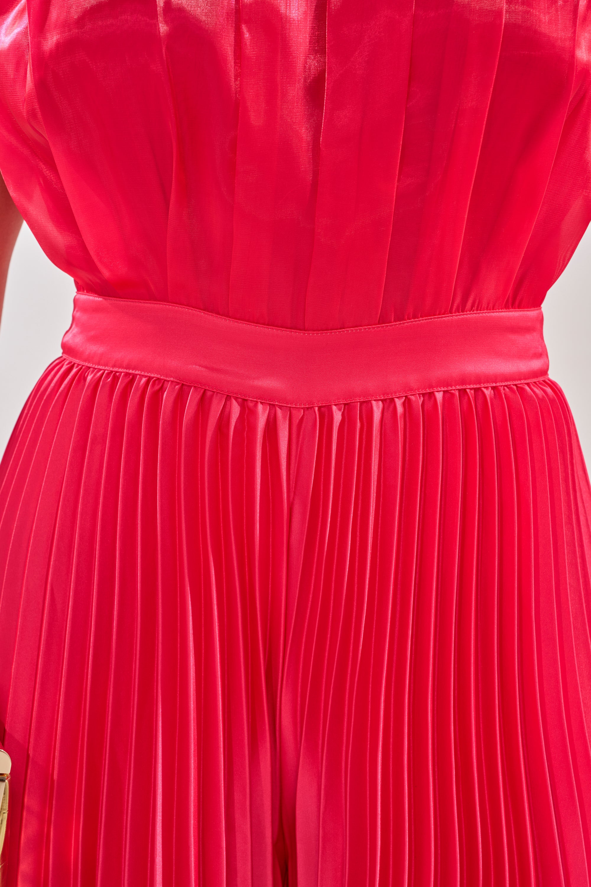 A close-up of a person wearing the SUNSET VIBES SATIN JUMPSUIT in vibrant pink, featuring pleats and a wide satin waistband that highlights the luxurious texture and detailing of the fabric. 4