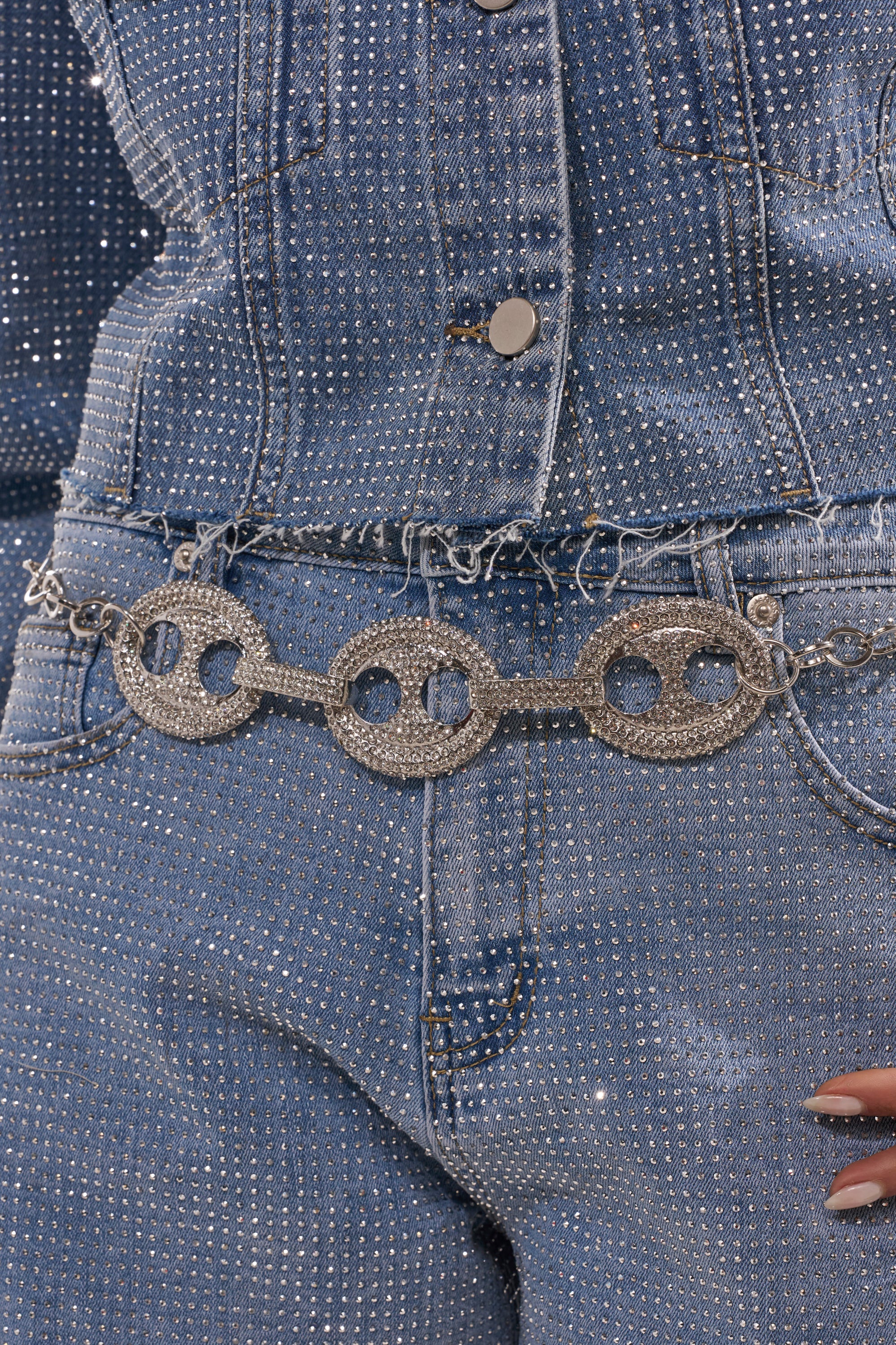A close-up shows a person in a sparkling denim jacket and jeans, accessorized with the CHAIN BELT featuring three handcuff-shaped links. Their manicured hand on their hip evokes iconic Y2K fashion vibes. 0