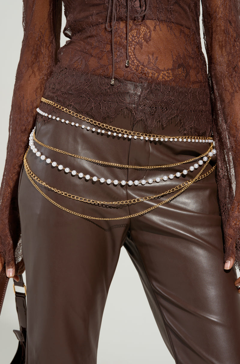 A person wearing a sheer, long-sleeved brown lace top and brown leather pants adorned with the PEARL PLEASE LAYERED CHAIN BELT, featuring adjustable lobster clasp closures.