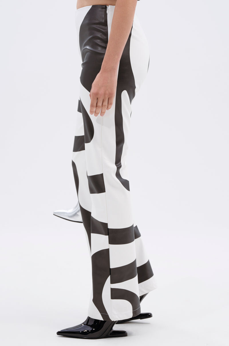 A person in profile wears the GROOVE ON FAUX LEATHER FLARE TROUSER, featuring a bold black-and-white graphic design and black pointed-toe shoes, set against a plain light background.