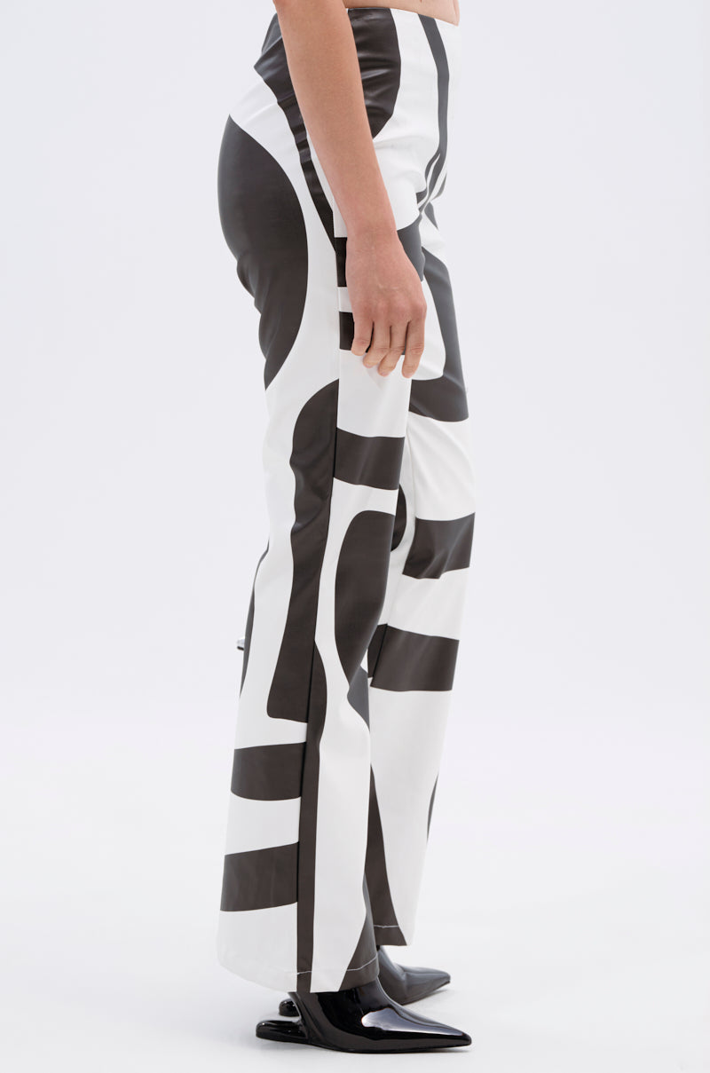 Only the lower torso and legs are visible as a person stands in profile wearing the GROOVE ON FAUX LEATHER FLARE TROUSER, featuring a high rise and abstract black and white pattern, paired with black pointed-toe shoes against a plain background.