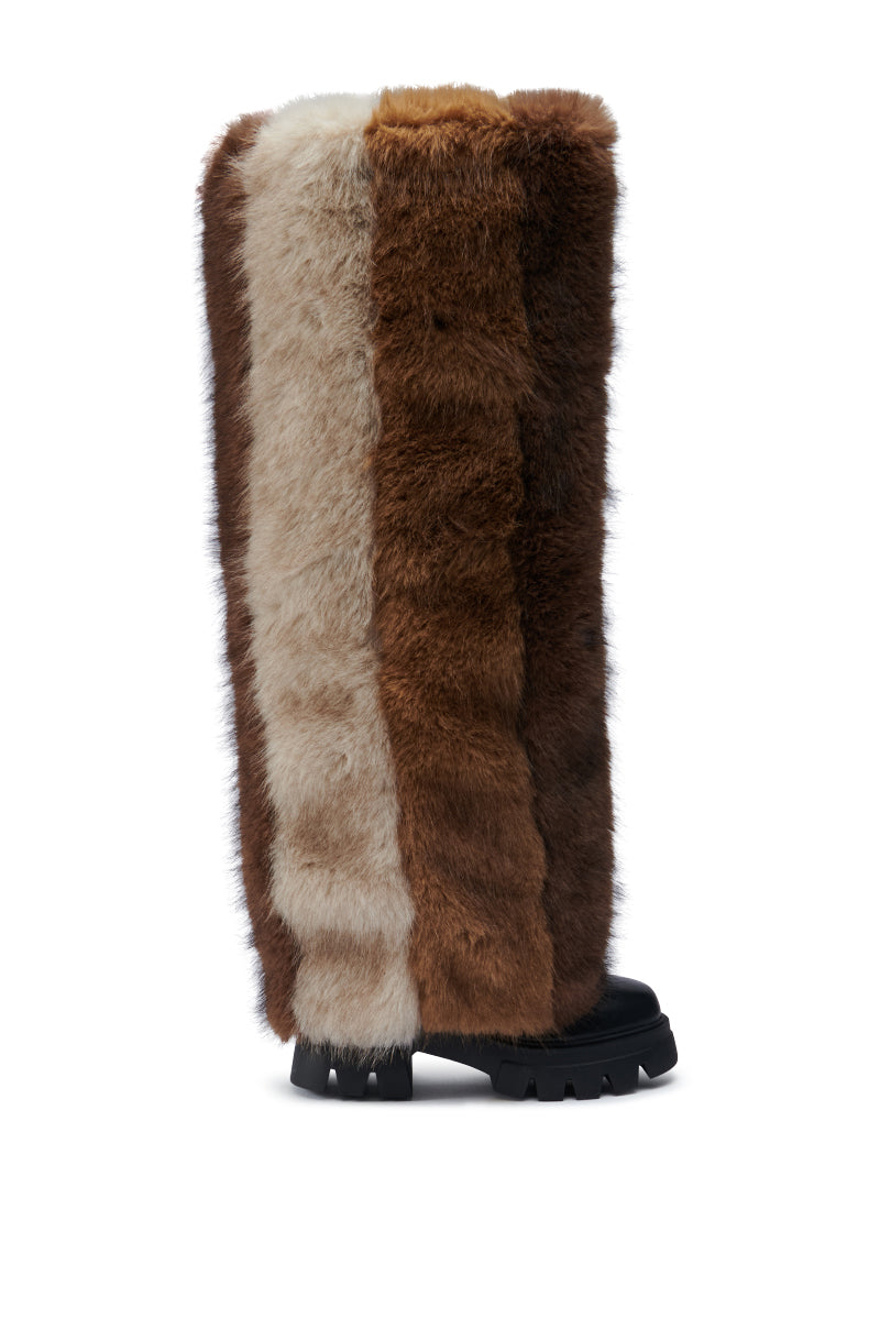 The AZALEA WANG JUBILANT BROWN MULTI BOOT features a pair of black-soled faux leather boots adorned with long faux fur strips in light beige, medium brown, and dark brown, forming a vertical striped pattern. These chunky heel boots make a striking impression against the plain white background.
