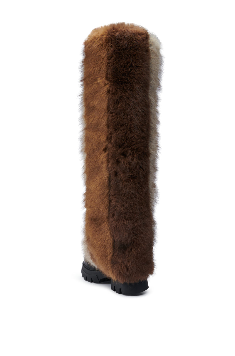 The AZALEA WANG JUBILANT BROWN MULTI BOOT is a tall boot featuring fluffy brown and grey fur with a black sole, designed with chunky heels, standing elegantly against a white background.