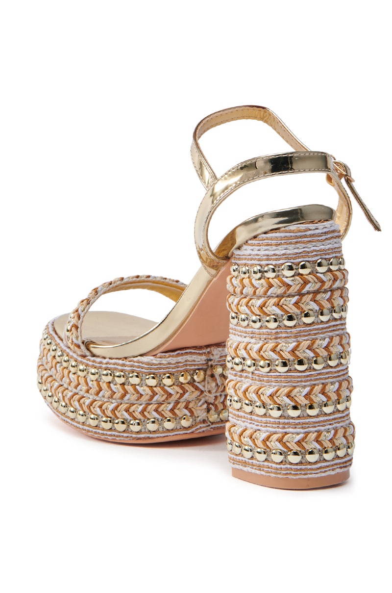 The AZALEA WANG JUDSON GOLD RAFFIA AND GEMS PLATFORM SANDAL features a chunky heel, multicolored braided detailing, and gold metallic straps. The ankle buckle ensures a perfect fit, while the textured heel and sole add chic elegance.