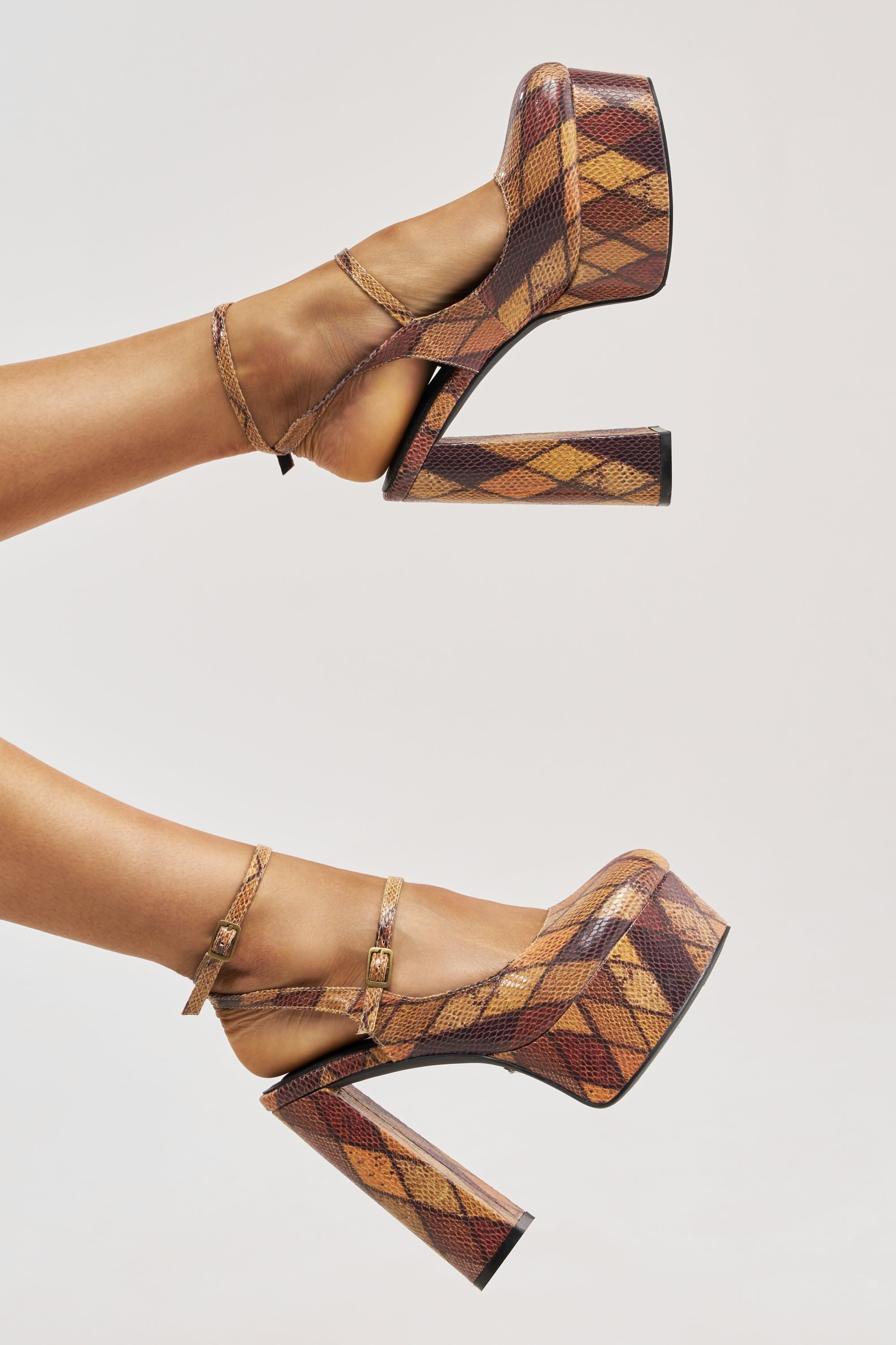 A pair of feet model the AZALEA WANG JULIARA MULTI PATTERNED PLATFORM PUMP—snakeskin print heels with brown and tan tones, ankle straps, and high platform block heels—set against a plain light background.