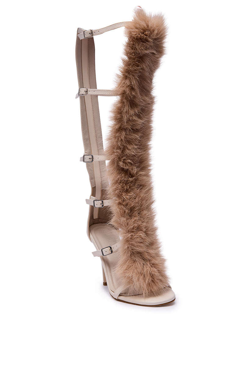 The AZALEA WANG JUSTYCE IVORY FUR GLADIATOR SANDAL is a tall beige sandal with multiple straps, buckles, and a vertical strip of fluffy light brown fur running up the front.