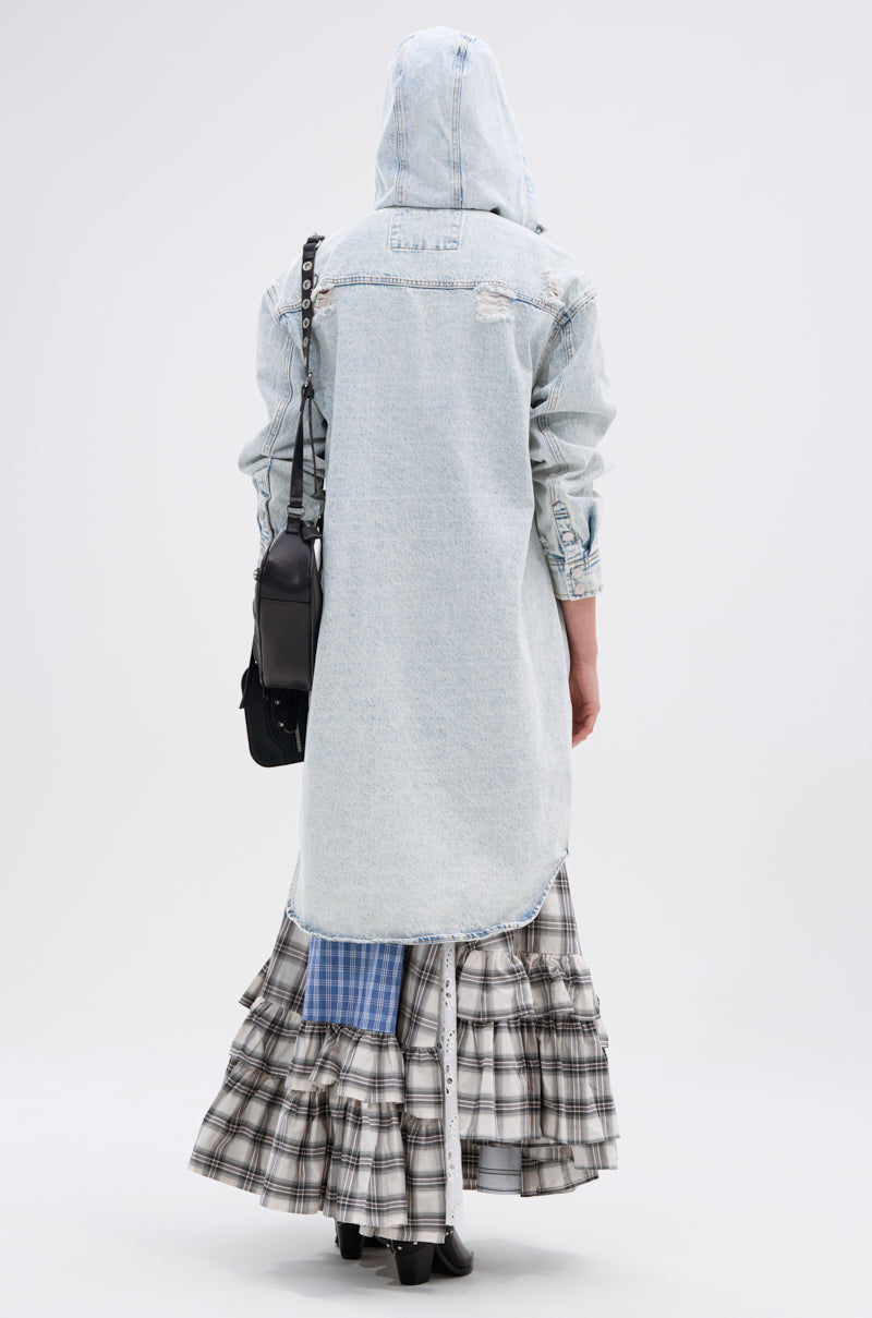 A person stands with their back to the camera, wearing the ZOEY HOODED DENIM JACKET over a tiered plaid skirt. They carry a black shoulder bag, wear black shoes, and pose against a plain light-colored background.