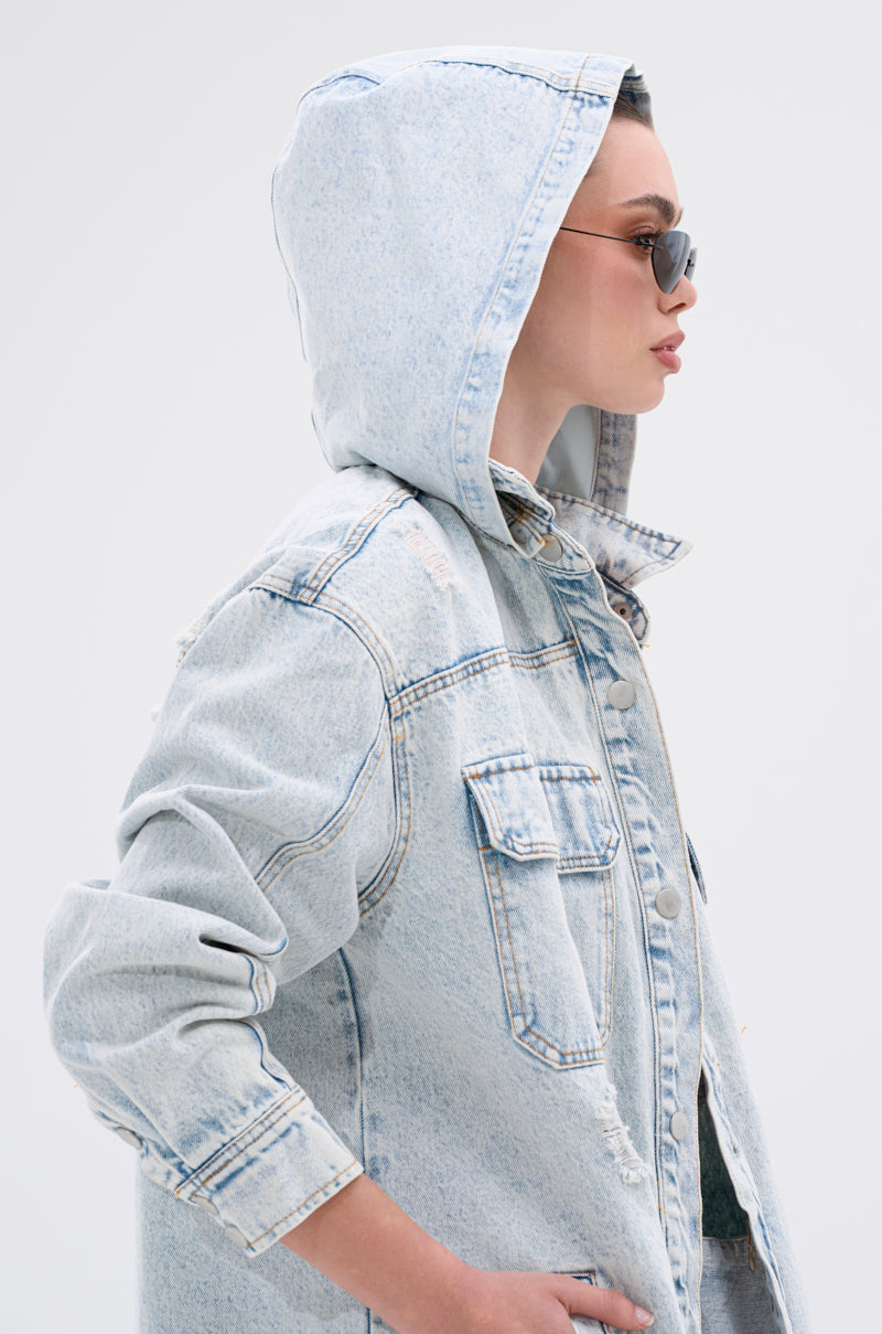 Wearing the ZOEY HOODED DENIM JACKET and sunglasses, a person poses in profile against a plain light background. The light denim gives their look a casual edge.