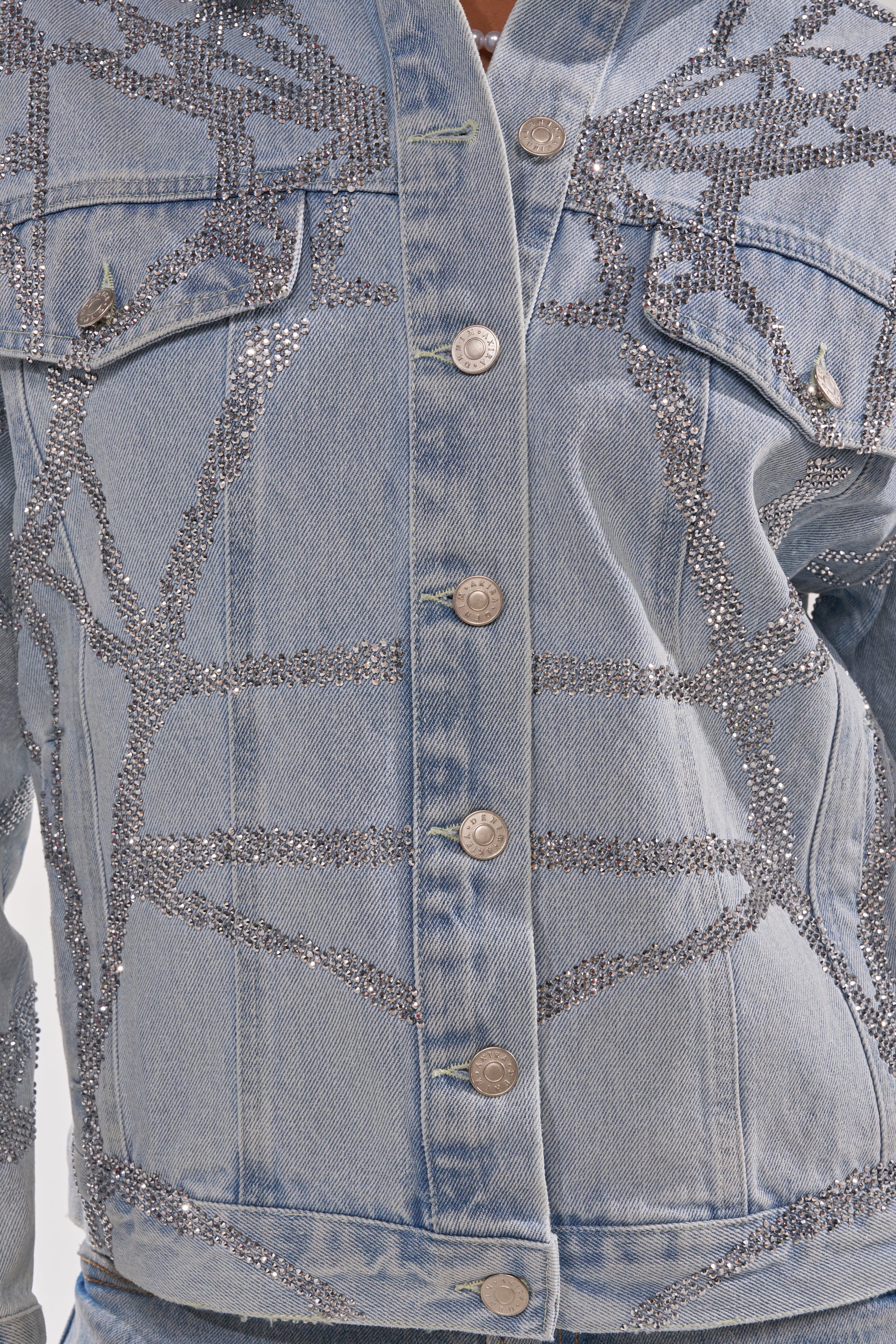 Close-up of the TWILIGHT ZONE RHINESTONE DENIM JACKET in light blue, featuring sparkling rhinestone abstract branch patterns, metallic buttons, and chest flap pockets on medium-wash denim. 9