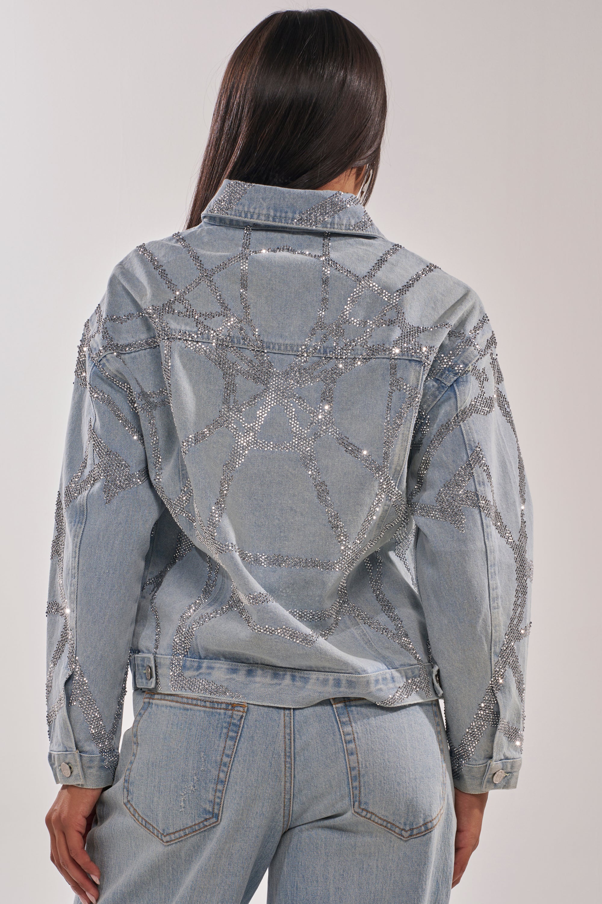 A woman faces away, wearing the TWILIGHT ZONE RHINESTONE DENIM JACKET—a medium-wash piece with silver rhinestones in geometric patterns on the back and sleeves. 6