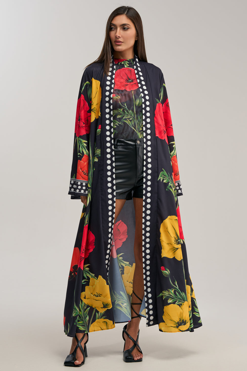 A woman models the BELLADONNA SATIN DUSTER, featuring bold red and yellow florals with white polka-dot borders, styled with a floral top, black high-waisted shorts, and strappy heels—the perfect date night look.