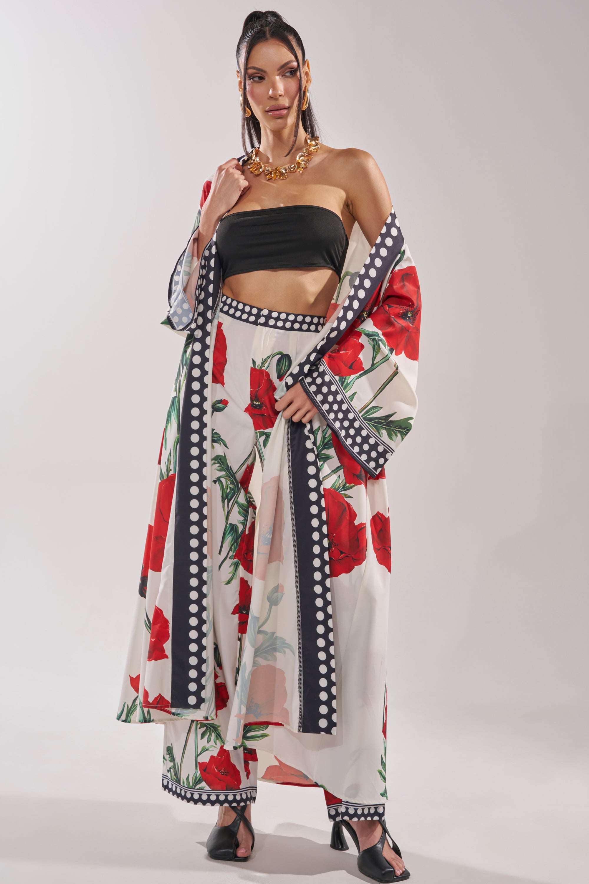 A woman poses in the BELLADONNA CHIFFON DUSTER, styled with matching wide-legged pants and a black bandeau top. She completes the look with black heels, gold jewelry, and a high ponytail.