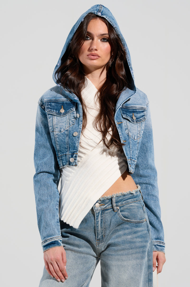 A person wearing the SITTING PRETTY FUR TRIM DENIM JACKET, featuring light blue denim with faux fur trim and hood, along with a white textured top, stands against a plain background. They have long brown hair and are styled in blue jeans.