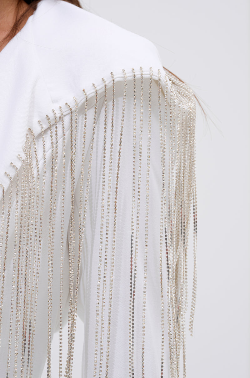A close-up of the DRIPPY RHINESTONE FRINGE BLAZER IN WHITE, showcasing long silver beaded fringe draping from the shoulder against a plain, light background. 11