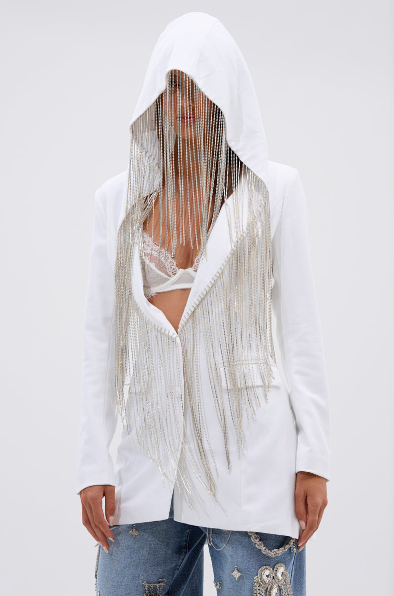 Wearing the DRIPPY RHINESTONE FRINGE BLAZER IN WHITE, featuring long silver fringe from the hood and a lace bralette underneath, they style it with embellished blue jeans for a bold, standout look. 3