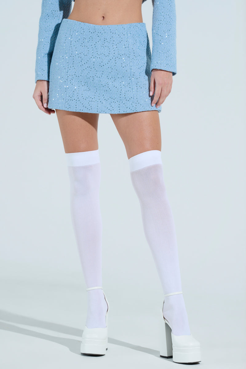 A person is wearing a light blue sequined two-piece outfit featuring the TEA FOR TWO TWEED SKORT and a long-sleeved top. Paired with white thigh-high socks and platform heels, the chic high-rise look stands out against a plain background, keeping the focus on their dazzling attire.
