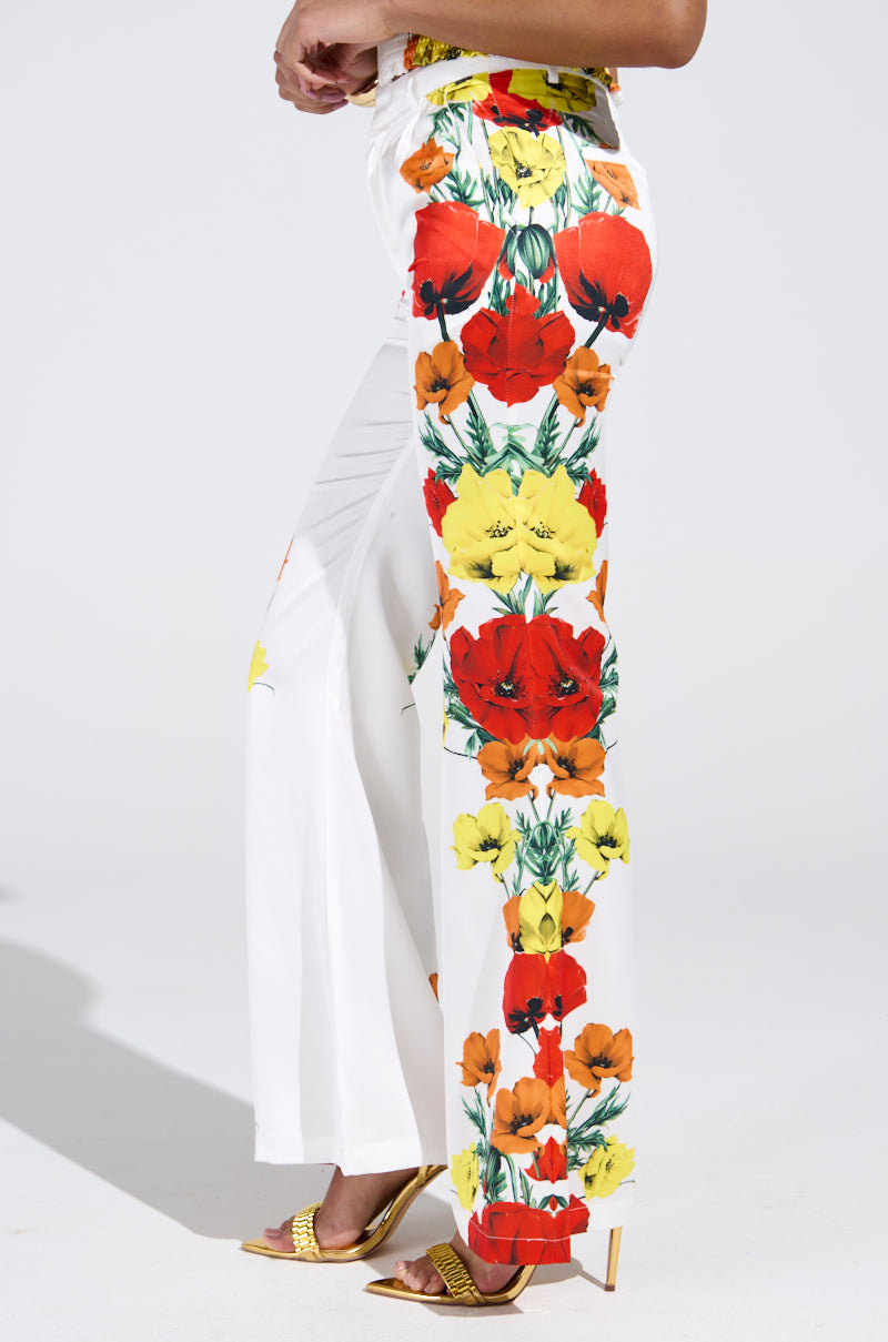 A person is wearing MIND MY OWN FLORAL SATIN TROUSERS, high-rise wide-leg style with photorealistic floral side prints, paired with yellow high-heeled sandals against a plain light background.